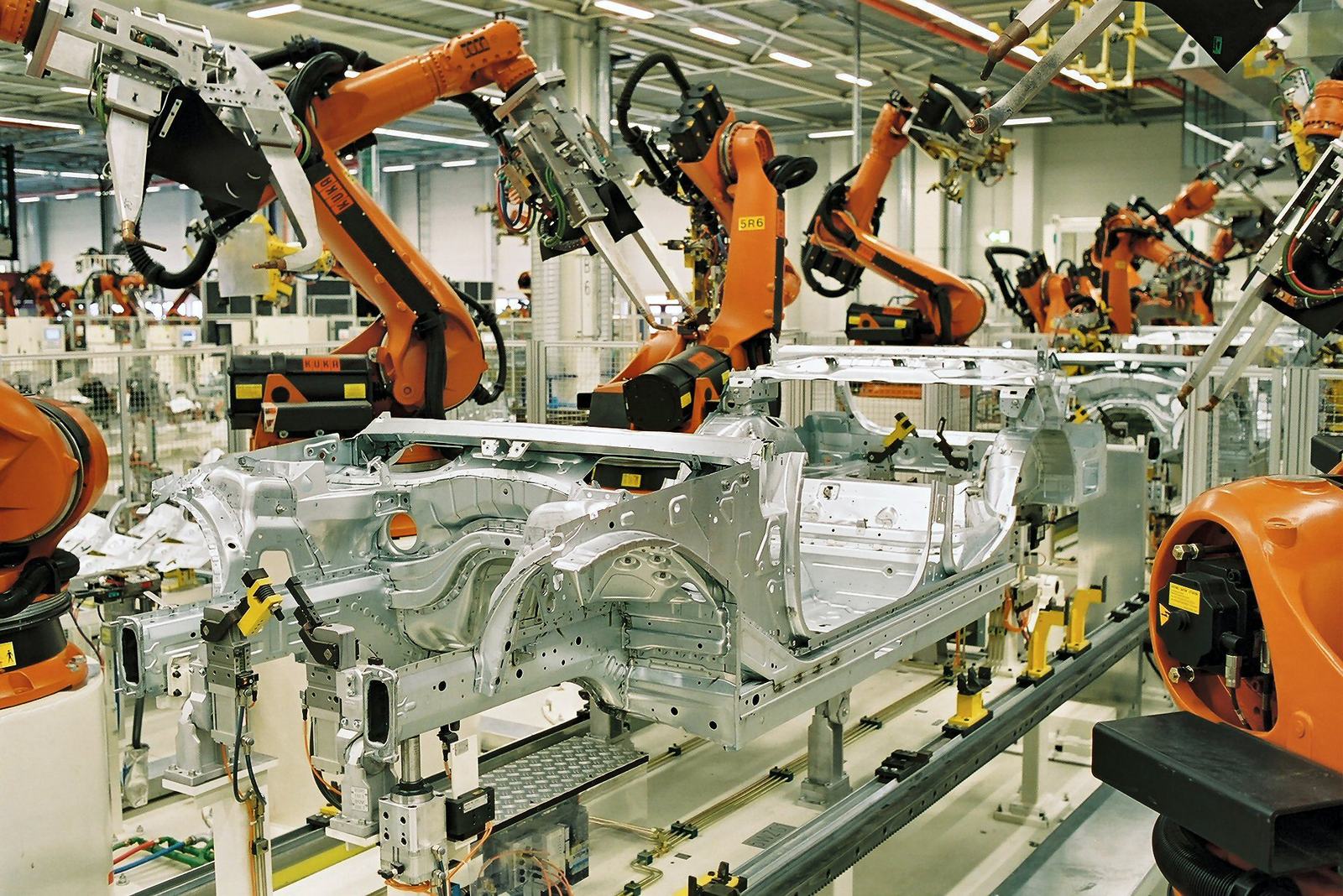 Row of orange KUKA six-axis industrial robots spot-welding car bodies on an automotive body-in-white line at BMW's Leipzig plant.